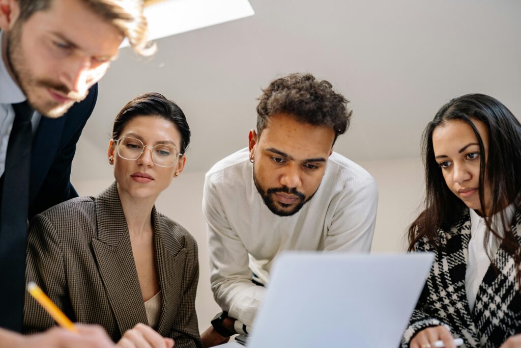 A diverse group of professionals collaborating on a project around a laptop in a modern office setting.