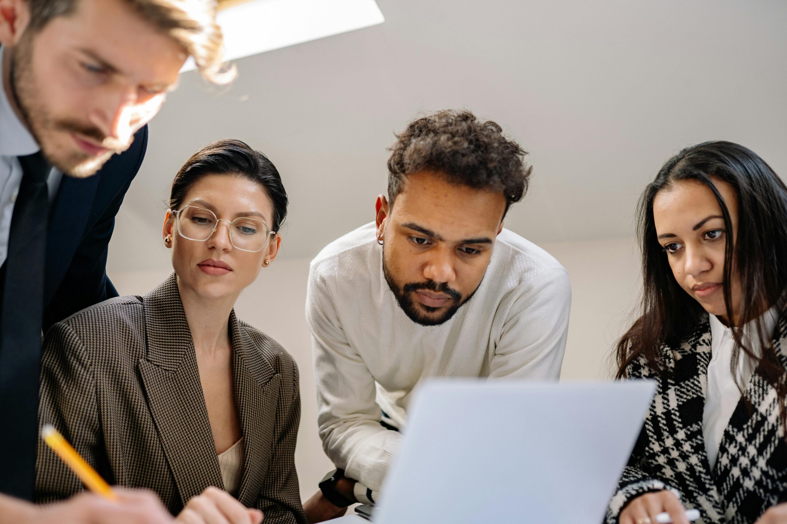 A diverse group of professionals collaborating on a project around a laptop in a modern office setting.